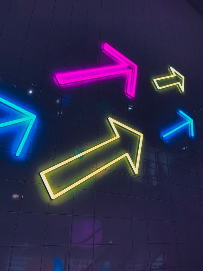 Multiple colorful neon arrow signs pointing in different directions against dark ceiling - accounting services for creative businesses exploring growth opportunities and strategic direction