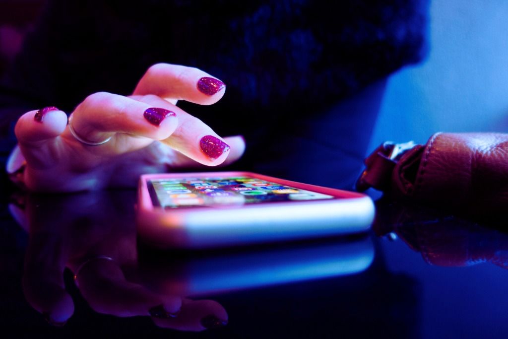 Hands with glittery nail polish using smartphone with blue and pink neon lighting - accounting services for beauty professionals and creative entrepreneurs