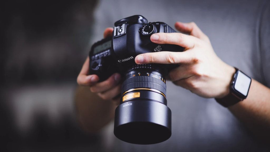 Hands holding professional DSLR camera with telephoto lens - accounting services for professional photographers and camera equipment businesses