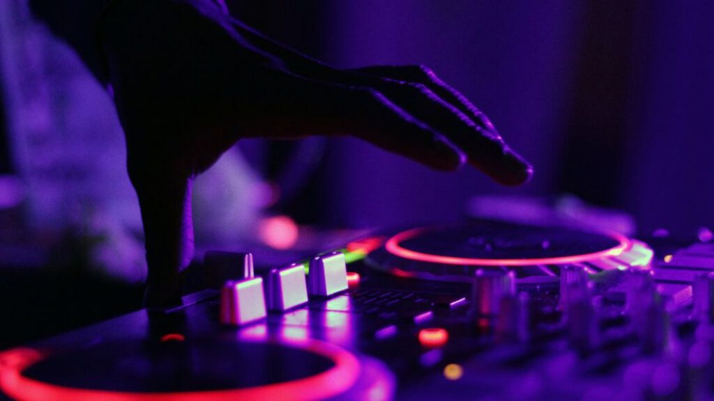 DJ hands operating turntable mixing console with purple and pink club lighting - accounting services for DJs and music entertainment professionals