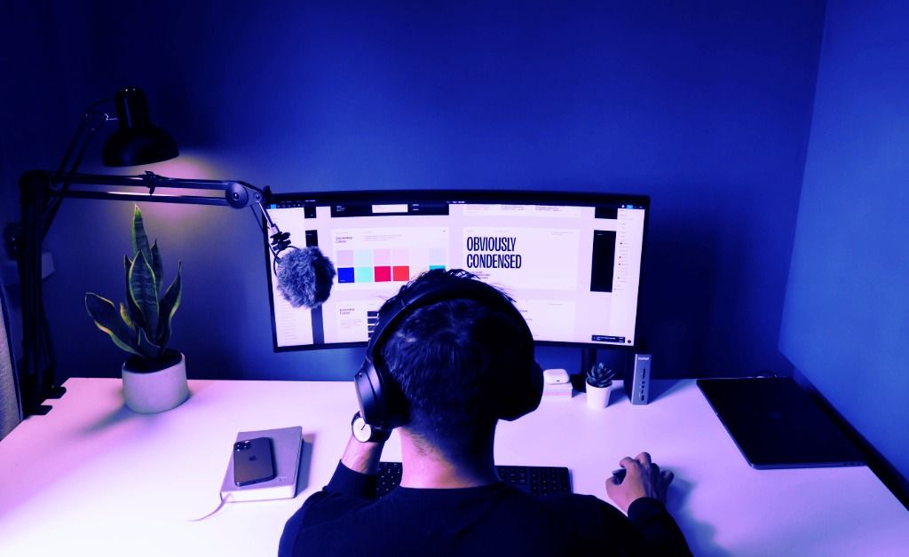 Designer working at computer with headphones in blue-lit home office workspace - accounting services for graphic designers and remote creative professionals