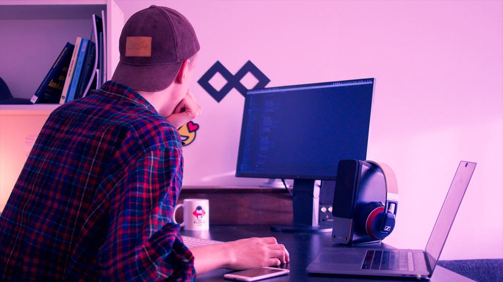 Young man in plaid shirt and cap working at dual monitor gaming setup with headset in pink-lit room - accounting services for content creators and gaming professionals