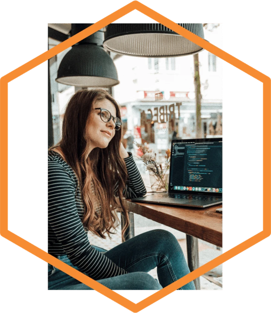 Woman with glasses coding on laptop in cafe workspace with pendant lighting in orange hexagonal frame - accounting services for web developers and freelance programmers