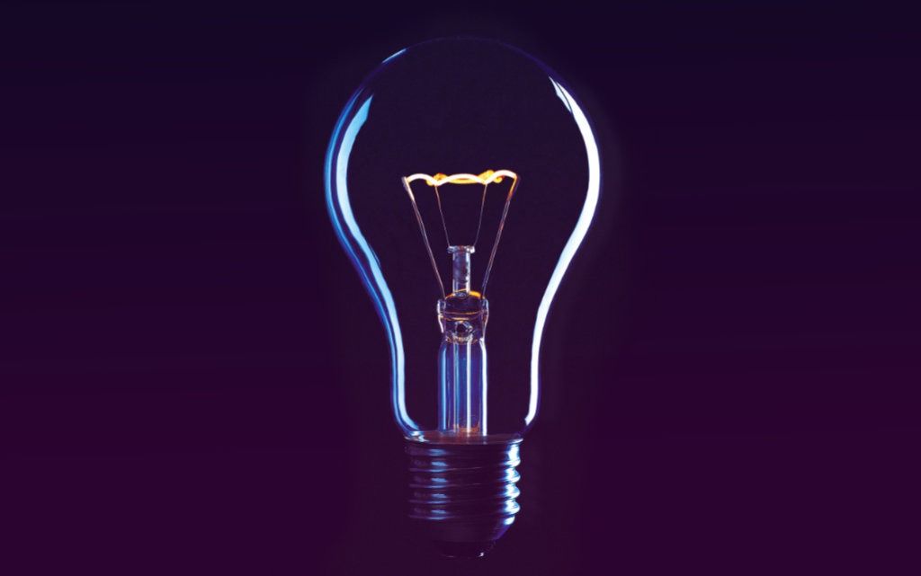 Illuminated light bulb with blue light effects on reflective surface against purple background - accounting services for innovative creative businesses and startup entrepreneurs