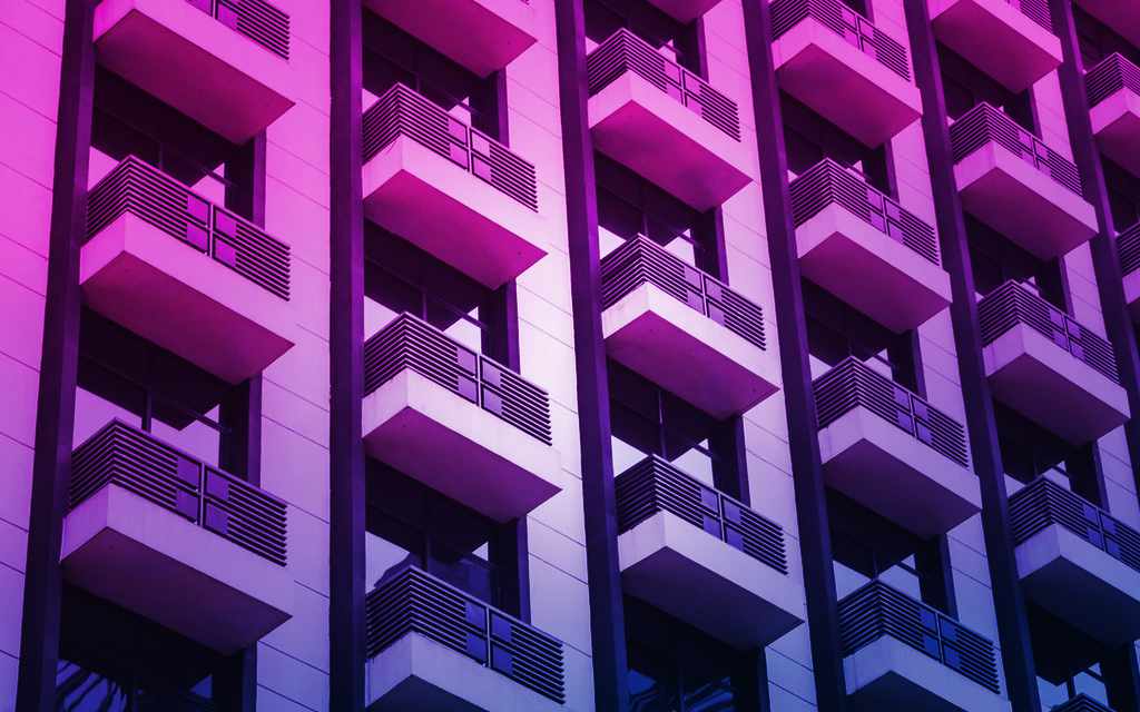 Modern apartment building facade with repeating balcony pattern in pink and purple lighting - accounting services for property developers and real estate creatives
