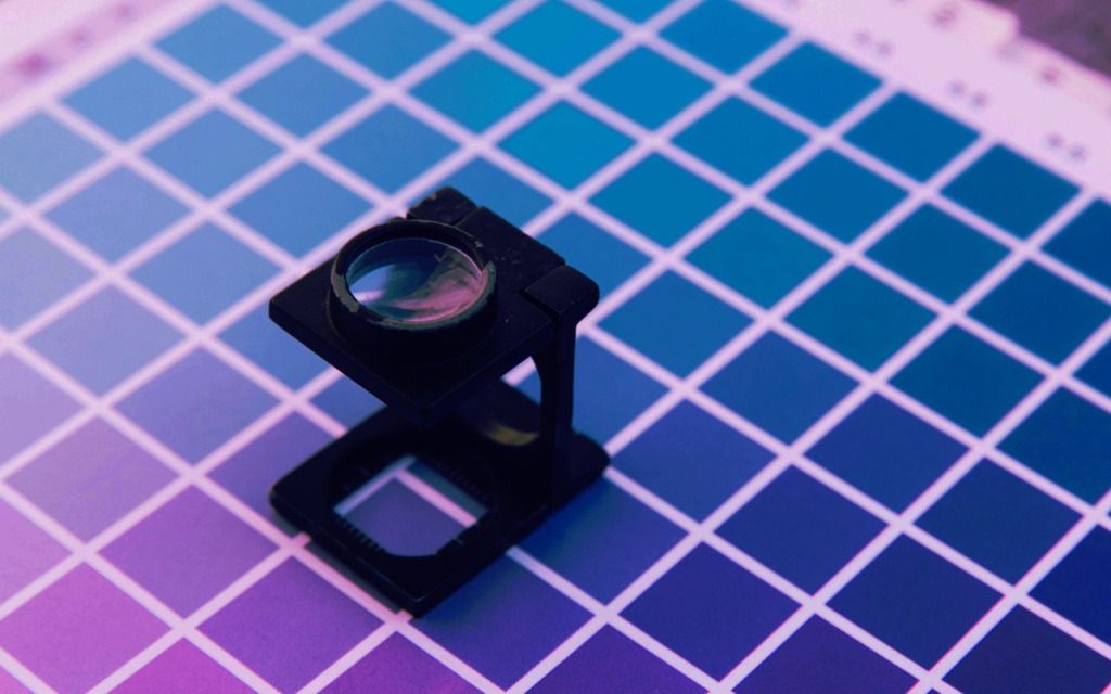 Black magnifying loupe on blue and purple color sample grid - accounting services for graphic designers and print professionals