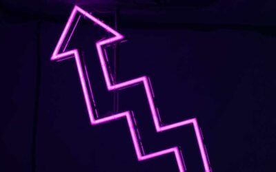 Pink neon upward arrow sign against dark background - accounting services for growing creative businesses and startups